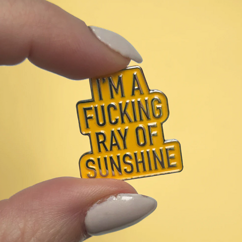 Enamel pin with text held by a hand against a yellow background