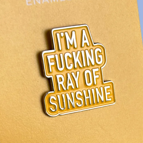 Enamel pin with text 'I'm a fucking ray of sunshine' on a beige background