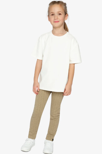 A young girl modeling a white short-sleeve crewneck t-shirt and beige ribbed leggings with white sneakers, standing against a light gray studio background.