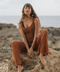 Woman sitting on a rock by the ocean wearing a brown ribbed outfit.
