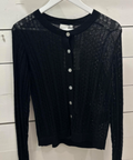 A black, long-sleeved, knitted top with a crew neck and button details, displayed on a white hanger against a wooden background.