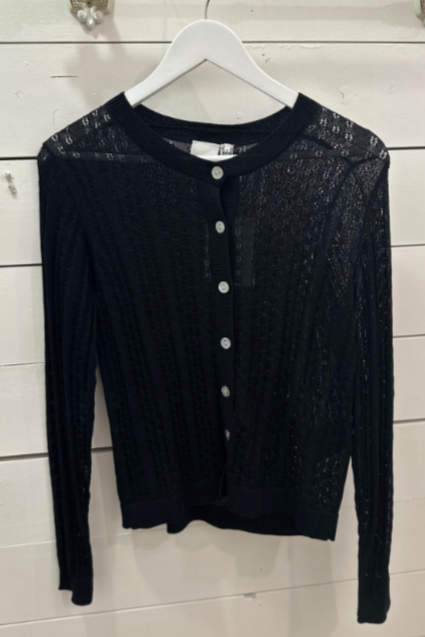 A black, long-sleeved, knitted top with a crew neck and button details, displayed on a white hanger against a wooden background.