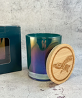 A white candle container with a black label that reads 'RavenSong' and 'FERN WOMAN'. The lid is off to the side, revealing a white candle inside.