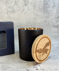 A white candle in a metal container with a label reading 'Sacred Smudge' on a light background.
