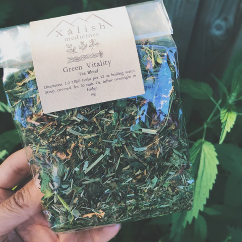 A clear packaging containing dried herbal tea leaves with a label reading 'Green Vitality Tea Blend' by Xalish Medicine.