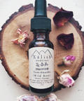 A bottle of 'Xalish Medicines' Wild Rose flower essence, placed on a wooden surface with dried rose petals around it.