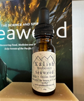 A bottle of Seaweed Flower Essence with a dropper, labeled Xalish Medicines, against a backdrop featuring a book with the title 'Seaweed'.