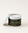 A white candle in a metal container with a label reading 'Sacred Smudge' on a light background.