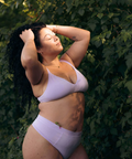 Woman in light purple bikini standing against a green leafy background