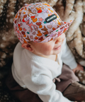 Baby wearing a colorful cap with animal patterns on a soft, patterned background