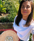 Woman holding a woven bag outdoors with greenery and flowers in the background