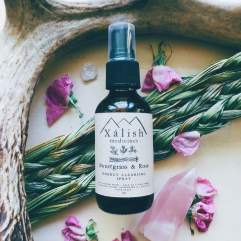 Xalish Sweetgrass & Rose energy cleansing spray bottle on a natural background with flowers and herbs.