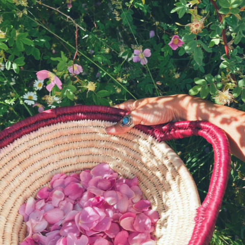 Person holding a woven basket with pink flowers against a green floral background