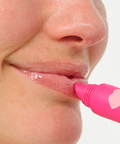 Person applying pink lip balm to their lips with a white background