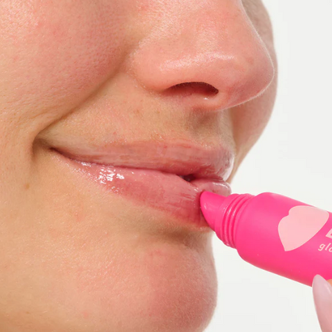 Person applying pink lip balm to their lips with a white background