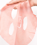 Pink face mask sheet held by a hand on a white background