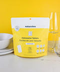Packaging of naturebee dishwasher tablets on a kitchen counter with dishes in the background.