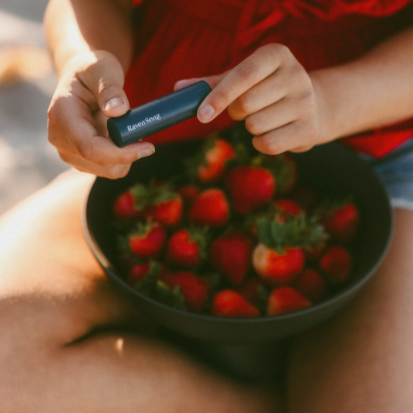 Person holding a bowl of strawberries with a product in their hand, outdoors.