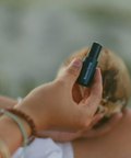 Person holding a black cylindrical object with a blurred natural background