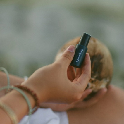 Person holding a black cylindrical object with a blurred natural background