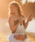 Woman holding a string bag with oranges by a lake at sunset