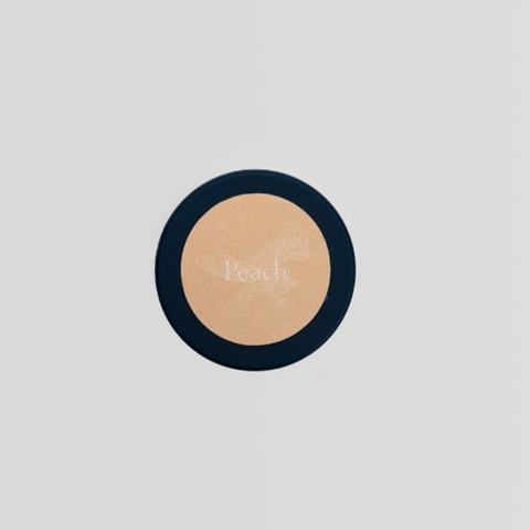 Round compact powder with peach color on a light gray background