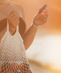 Person holding a phone and a white mesh bag with a warm, blurred background
