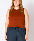 Woman wearing a rust-colored sleeveless top and dark blue pants against a plain background