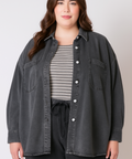 Woman wearing a dark denim jacket over a striped shirt on a plain background