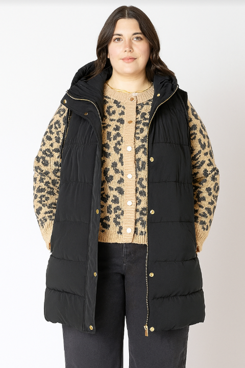 Person wearing a black puffer vest over a leopard print shirt on a white background