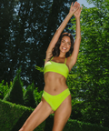 Woman in a bright green bikini posing outdoors with trees in the background