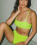 Woman wearing a bright green bikini sitting against a neutral background