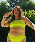 Woman in a bright green bikini standing outdoors with trees in the background