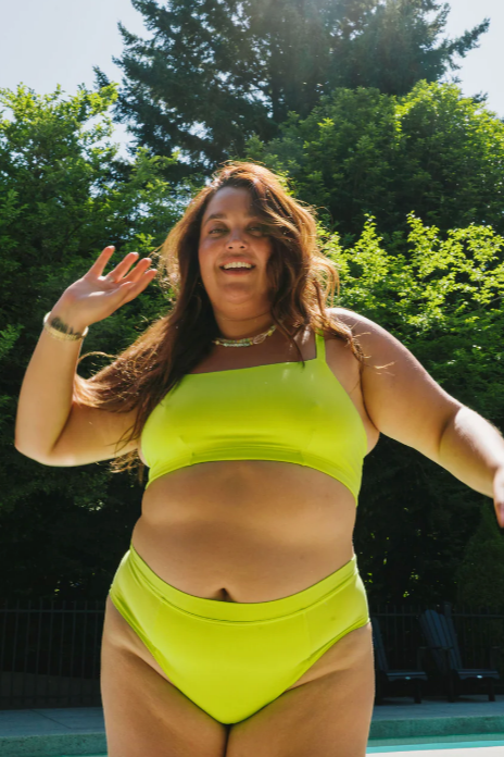 Woman in a bright green bikini standing outdoors with trees in the background