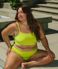 Woman in a bright green bikini sitting on stone steps outdoors