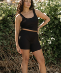 Woman wearing a black athletic outfit standing outdoors with greenery in the background