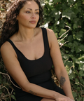Woman in a black sleeveless top sitting among green foliage