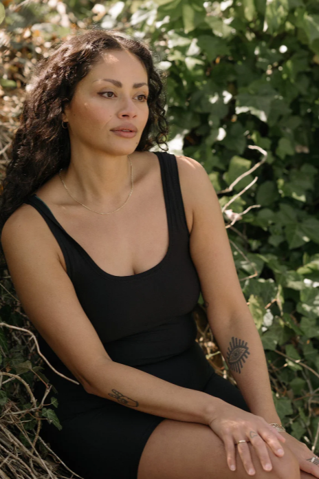 Woman in a black sleeveless top sitting among green foliage