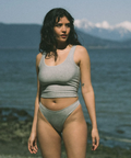 Woman in a gray bikini standing on a beach with mountains in the background