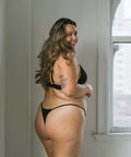 Woman wearing black lingerie standing in a room with a window in the background