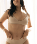 Woman wearing a beige bra and panties set against a light background