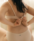 Woman wearing a beige bra and underwear set against a neutral background