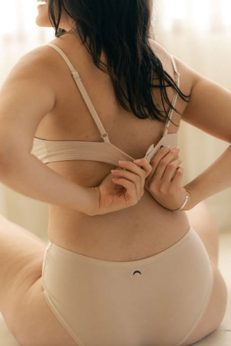 Woman wearing a beige bra and underwear set against a neutral background