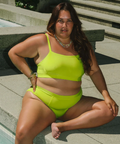 Woman in a bright green bikini sitting by a pool.