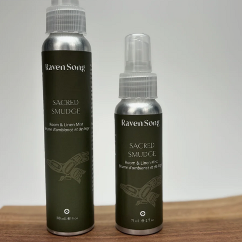 Two bottles of Raven Soap Sacred Smudge on a wooden surface with a gray background.