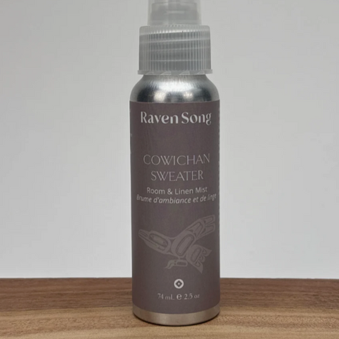 Raven Song Cowichan Sweater room & linen mist bottle on a wooden surface with a gray background