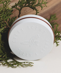 White jar with a brown lid on a white surface with greenery