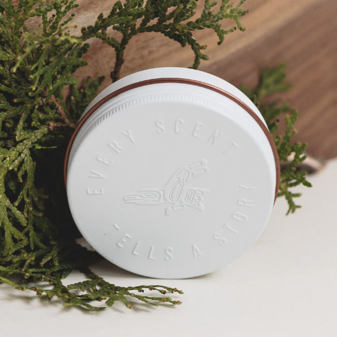 White jar with a brown lid on a white surface with greenery