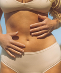 Person wearing a beige bikini against a clear blue sky.