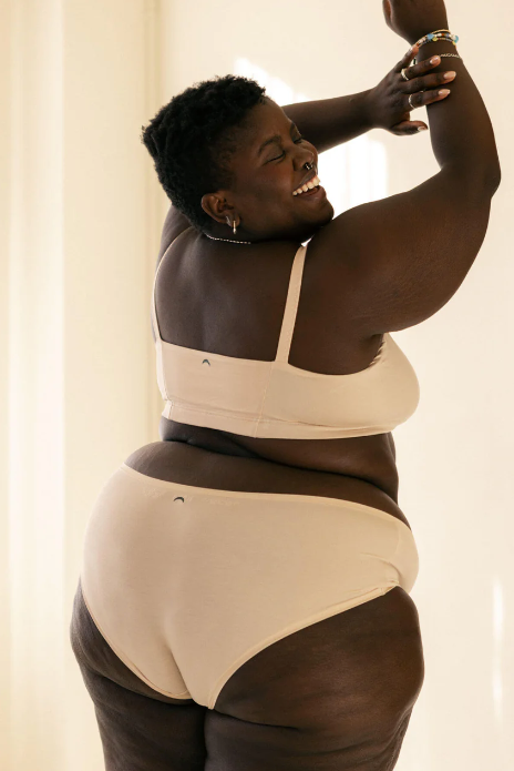 Person wearing a beige and black bodysuit against a neutral background